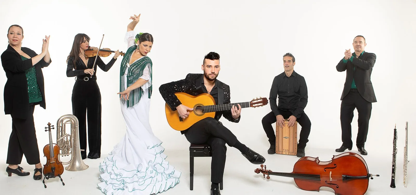 Foto oficial de la Daniel Martinez Flamenco Company: bailaora con bata de cola blanca, guitarrista, violinista, violonchelo, cajón y palmeros sobre fondo blanco.