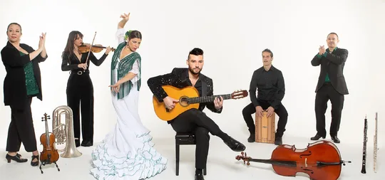 Foto oficial de la Daniel Martinez Flamenco Company: bailaora con bata de cola blanca, guitarrista, violinista, violonchelo, cajón y palmeros sobre fondo blanco.