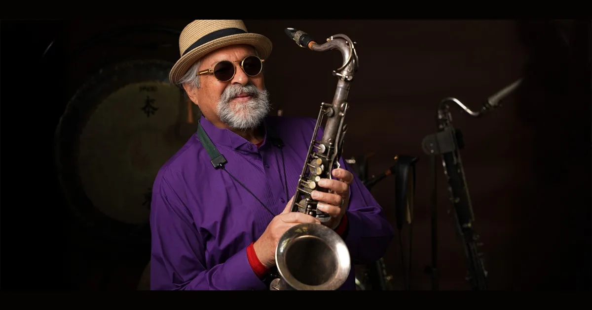 Foto oficial de Bozar para Coltrane 100: el saxofonista Joe Lovano, con sombrero y camisa morada, sostiene su saxofón tenor sobre fondo oscuro.